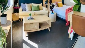 A modern living room with a sofa, coffee table, and a bed with a nightstand. There are plants and artwork on the walls. - Larger Room In Parap, saltwater pool, close to markets, Great coffee, Central. (Parap)