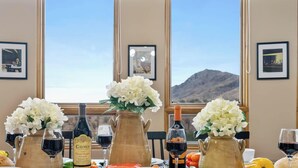 A table set with wine bottles, glasses, and flowers, with a mountain view through large windows.