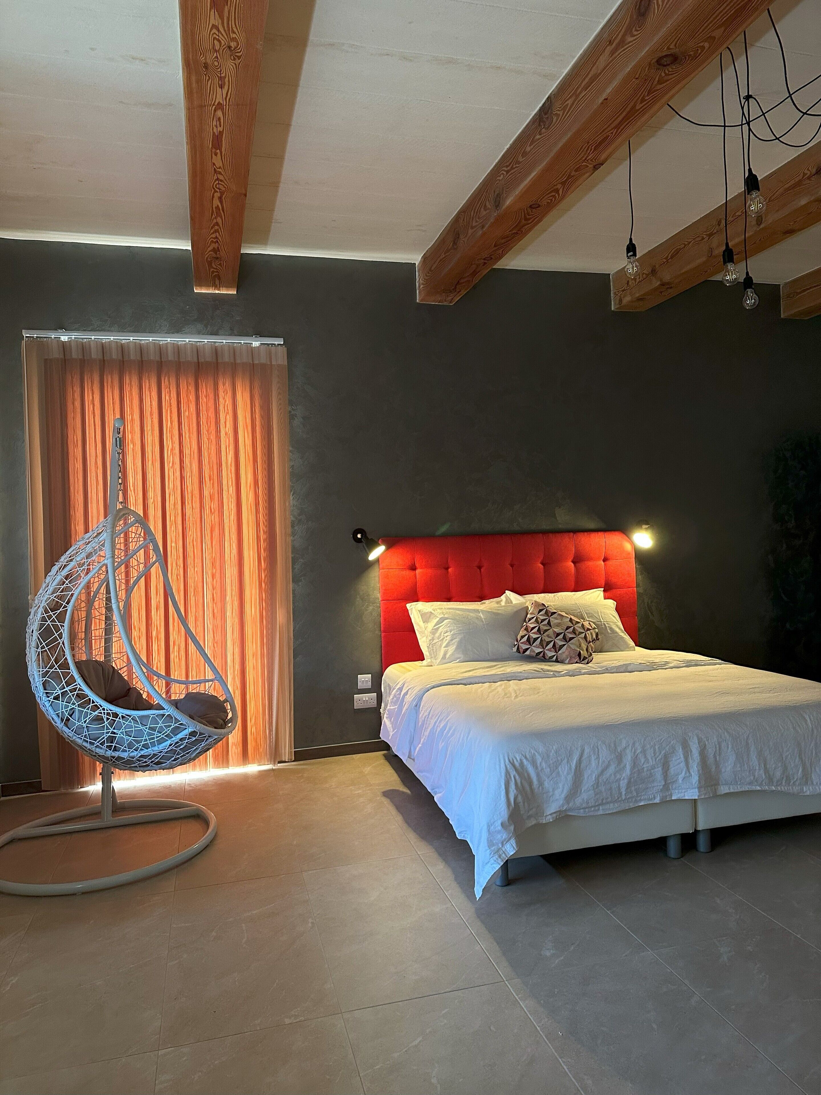 A bedroom with a bed, a hanging chair, and a red headboard.