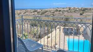 A balcony with two white chairs, a pool, and a view of the landscape. - Sea Holly Gozo (Nadur)