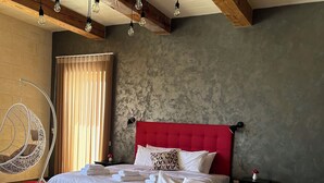 A hotel room with a large bed, a hanging chair, and a red headboard. - Sea Holly Gozo (Nadur)