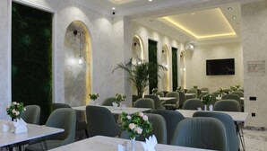 A conference room with multiple tables and chairs, a large screen, and a green wall with a plant. - Modern Hotel (Tashkent)