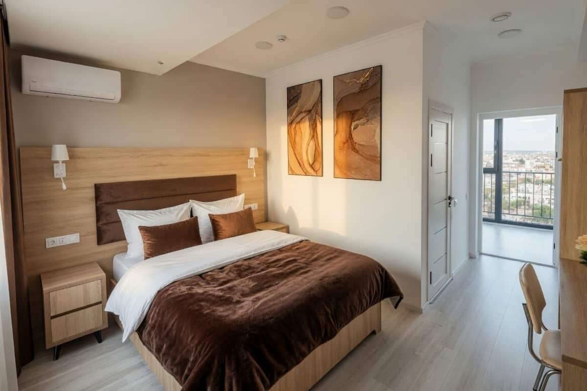 A modern bedroom with a wooden headboard, a large bed, bedside tables, a desk, and a view through a large window.