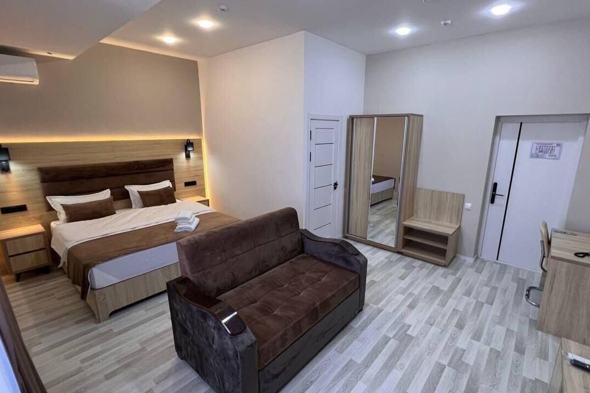 A modern hotel room with a bed, a sofa, a wardrobe, and a desk.