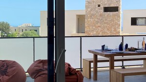 Een balkon met een stenen muur, een houten tafel met stoelen en twee loungestoelen.