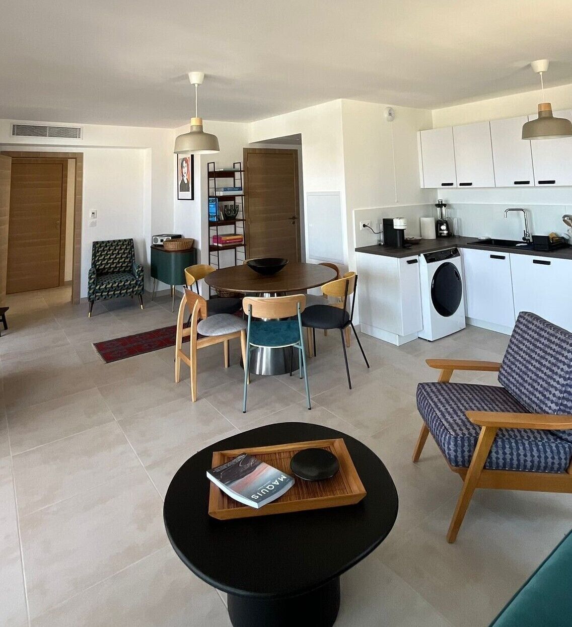 A modern living room with a dining area, a kitchen, and a laundry area.