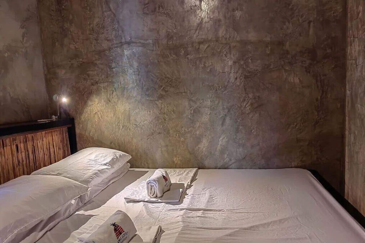 Habitación de hotel con una cama grande, dos almohadas, una colcha impecable y una lámpara de pared.