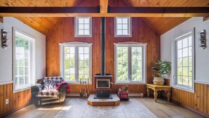 A cozy room with wooden walls, a fireplace, large windows, and a plaid chair.