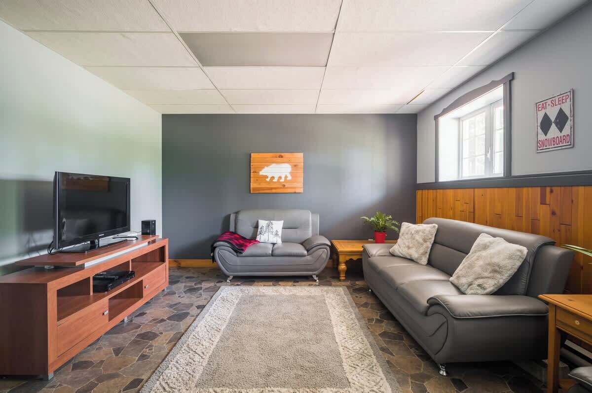 A living room with a television, a sofa, a couch, a rug, and a wall-mounted sign.