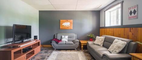A living room with a television, a sofa, a couch, a rug, and a wall-mounted sign.