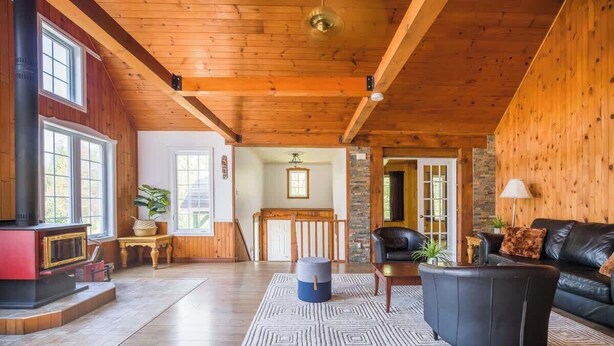 A spacious living area with a fireplace, a black leather sofa, and a wooden ceiling.