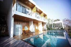 Un bâtiment moderne à deux étages doté d’une piscine, d’une terrasse en bois et d’un espace de détente extérieur.