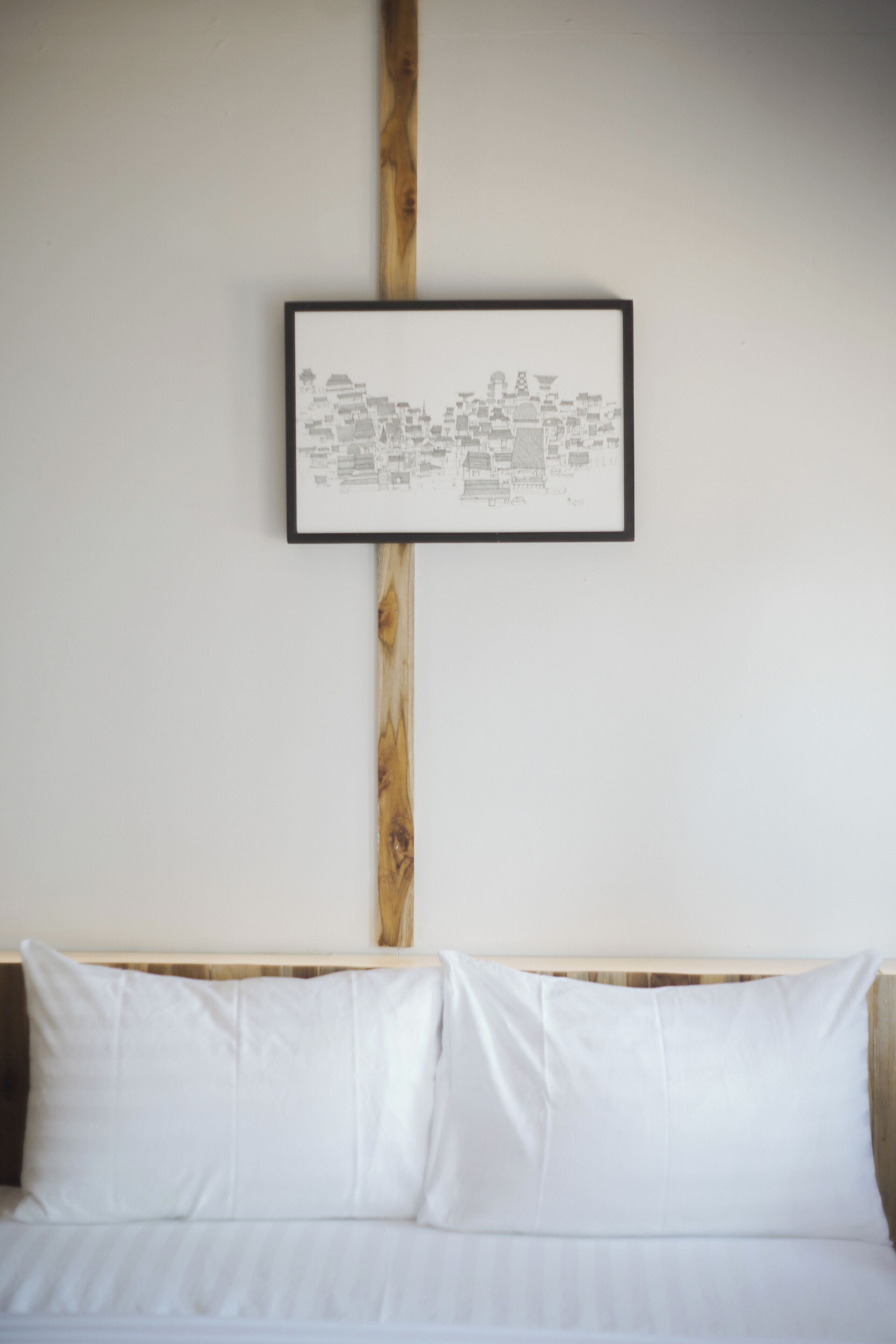 Desenho arquitetônico emoldurado na parede acima de uma cama com roupa de cama branca.