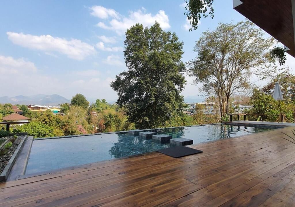 A wooden deck with a swimming pool, surrounded by trees and a view of distant mountains.