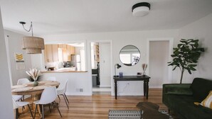 A modern living room with a green sofa, a dining table with chairs, a kitchen in the background, and a large mirror on the wall. - Yellowbird Retreat of Walla Walla Valley (College Place)