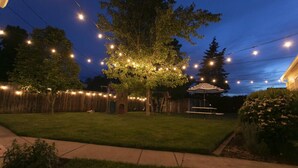 A backyard with a tree, string lights, a wooden fence, and a covered patio area. - Yellowbird Retreat of Walla Walla Valley (College Place)