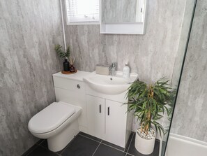 Un baño moderno con un inodoro blanco, un lavabo con espejo y una planta en maceta.