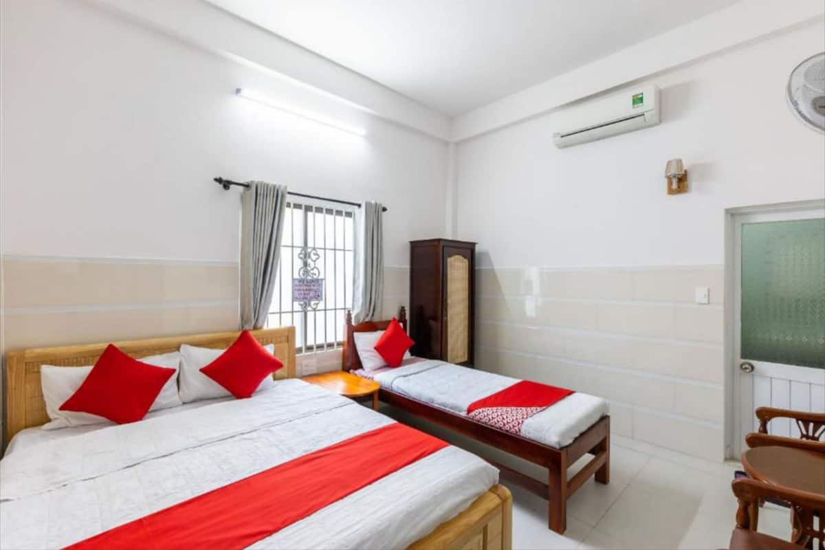 A hotel room with two beds, a wooden wardrobe, a small table, and an air conditioning unit.