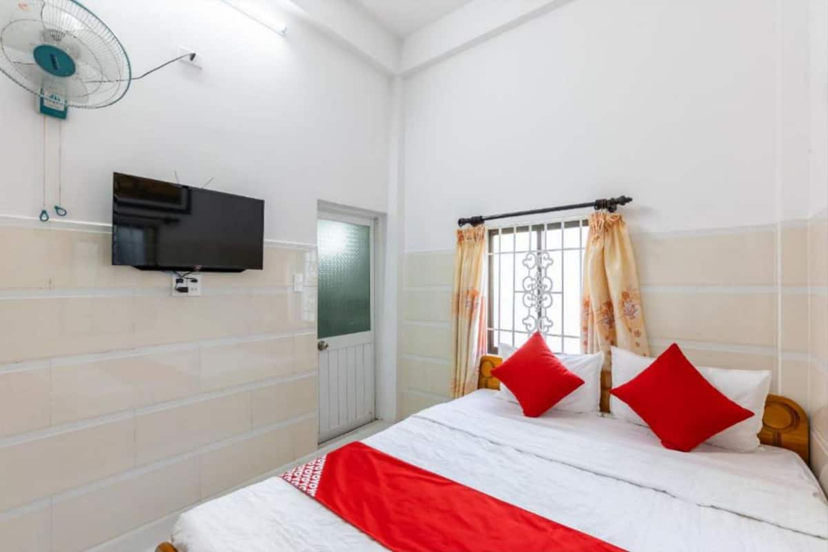 A bedroom with a bed, a TV mounted on the wall, a window with curtains, and a door.