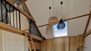 Un espace de vie de style loft avec un escalier en bois, un coin repas avec des chaises en osier, une table basse ronde en bois et un canapé bleu.