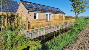 Une maison dotée de panneaux solaires, d’une terrasse en bois et située au bord d’une rivière.
