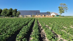 Un grand bâtiment doté de panneaux solaires, avec un champ de cultures devant.