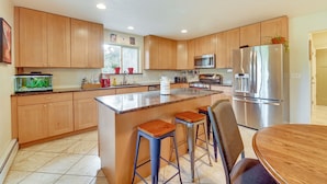 A modern kitchen with wooden cabinets, a stainless steel refrigerator, a microwave, and a large island with bar stools. - Lovely Soldotna Home, Steps From Kenai River (Soldotna)