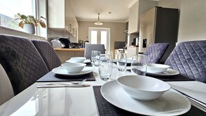 Un coin repas moderne avec une table dressée pour quatre personnes, comprenant des assiettes, des bols, des verres et des couverts.