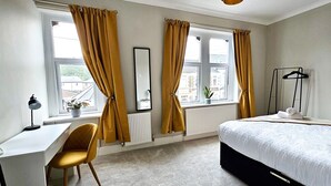 Une chambre à coucher comprenant un lit, un bureau, une chaise, un radiateur et une fenêtre avec des rideaux.