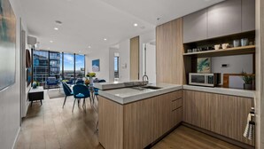 A modern kitchen with wooden cabinets, a built-in microwave, and a large window overlooking a cityscape. - Premium Chic: A Relaxing Retreat (Port Melbourne)