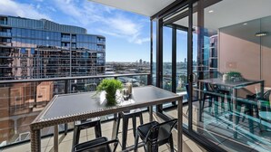 A balcony with a table and chairs, a potted plant, and a city view. - Premium Chic: A Relaxing Retreat (Port Melbourne)