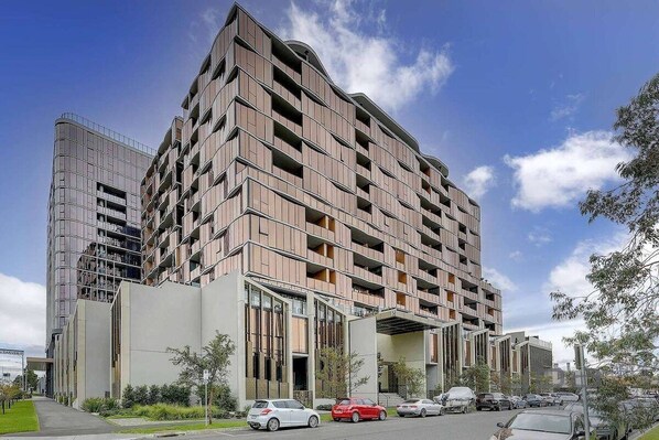 A multi-story residential building with a modern design, featuring balconies and a mix of glass and wood paneling.
