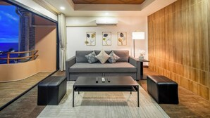 Un salon moderne avec un canapé gris, des poufs noirs, une table basse et des œuvres d’art accrochées au mur.