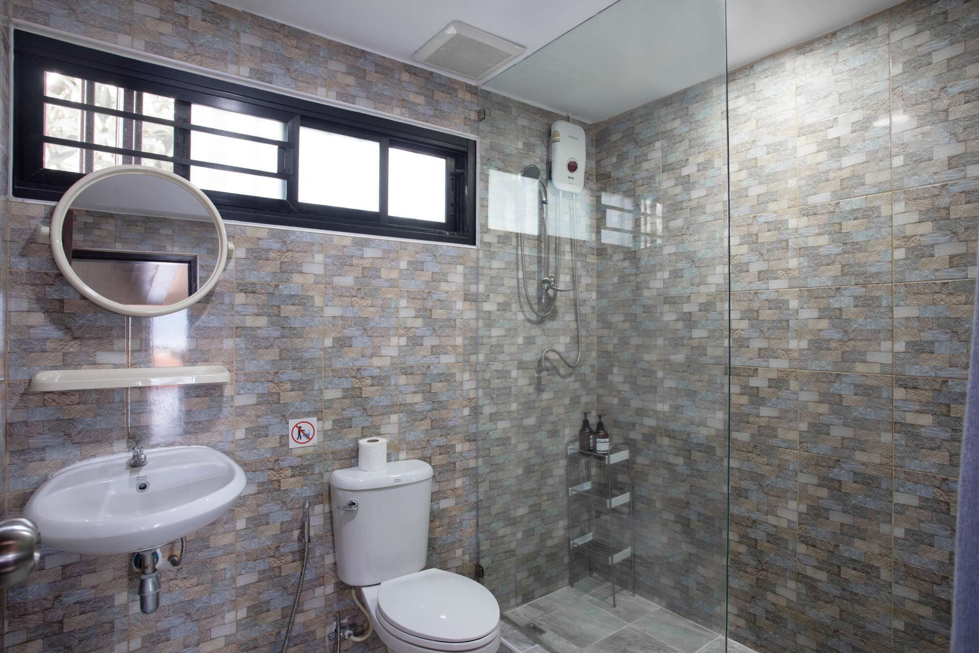Un bagno con parete doccia piastrellata, un WC, un lavandino e una finestra sopra il lavandino.