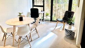 Una habitación moderna con una mesa redonda, sillas blancas, una silla negra y una mesita auxiliar con una planta.