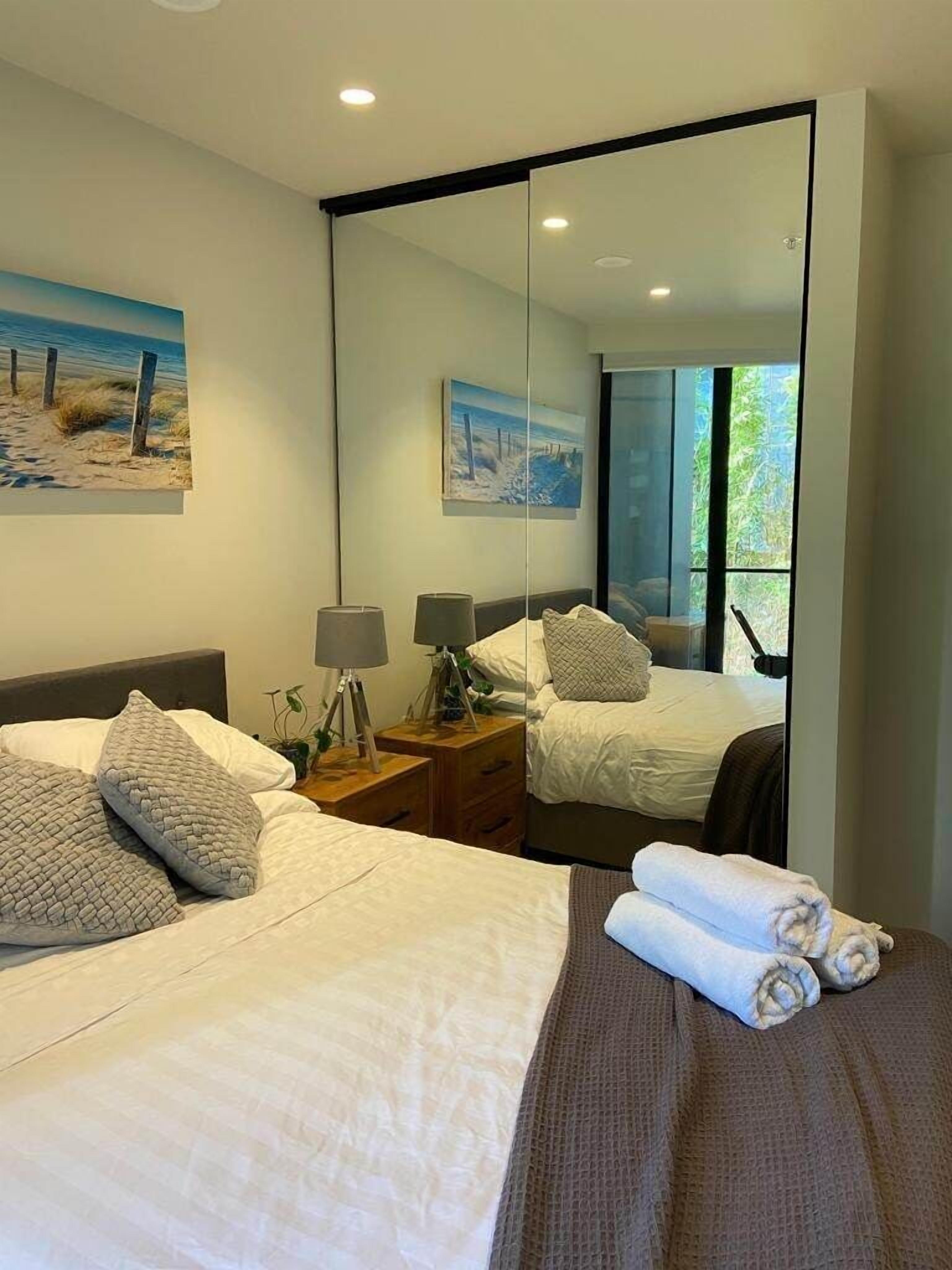 A hotel room with a large bed, a bedside table with lamps, a mirror, and a painting on the wall.
