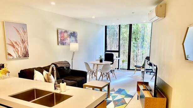 Una cocina moderna con una isla central, un comedor con mesa y sillas, y vistas al exterior a través de amplios ventanales.