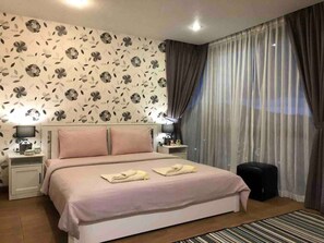 A neatly arranged bedroom with a bed, nightstands, a small table, and a window with curtains.