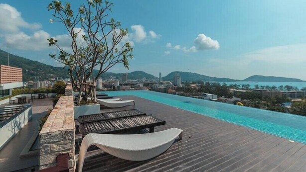 A rooftop infinity pool with lounge chairs and a tree, overlooking a cityscape and mountains. - ✈Sea-view 80sqm-1 Bedroom Home-Patong Beach (Tambon Patong)
