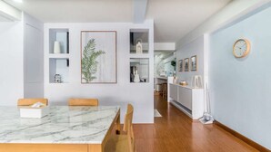 A modern dining area with a marble table, wooden chairs, and a kitchen in the background.