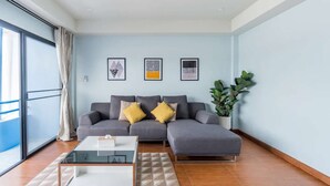 A modern living room with a grey sectional sofa, a glass coffee table, and a potted plant.