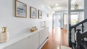 A hallway with a white console table, framed artwork, and a staircase with a black railing.