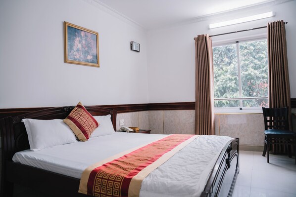 A neatly made bed with a patterned bedspread, a bedside table with a lamp, and a window with curtains.