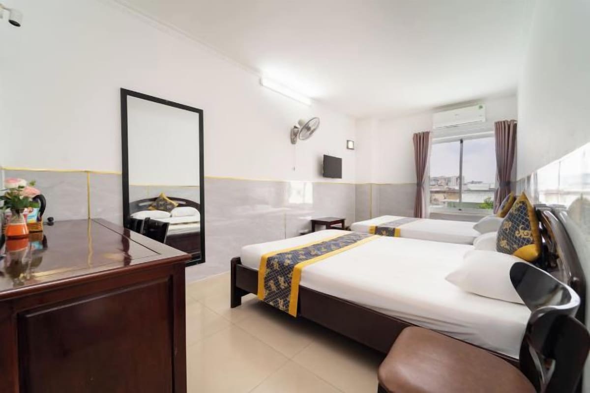 A hotel room with a bed, a desk, a mirror, a window, and a view of the city.