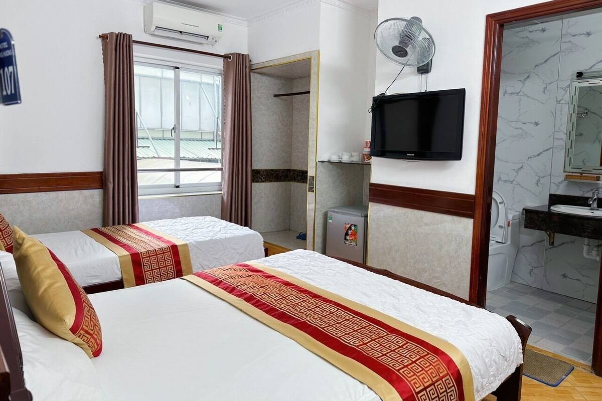 Ein Hotelzimmer mit zwei Betten, einem Fernseher, einem Ventilator, einem Badezimmer mit Spiegel und Blick ins Freie.