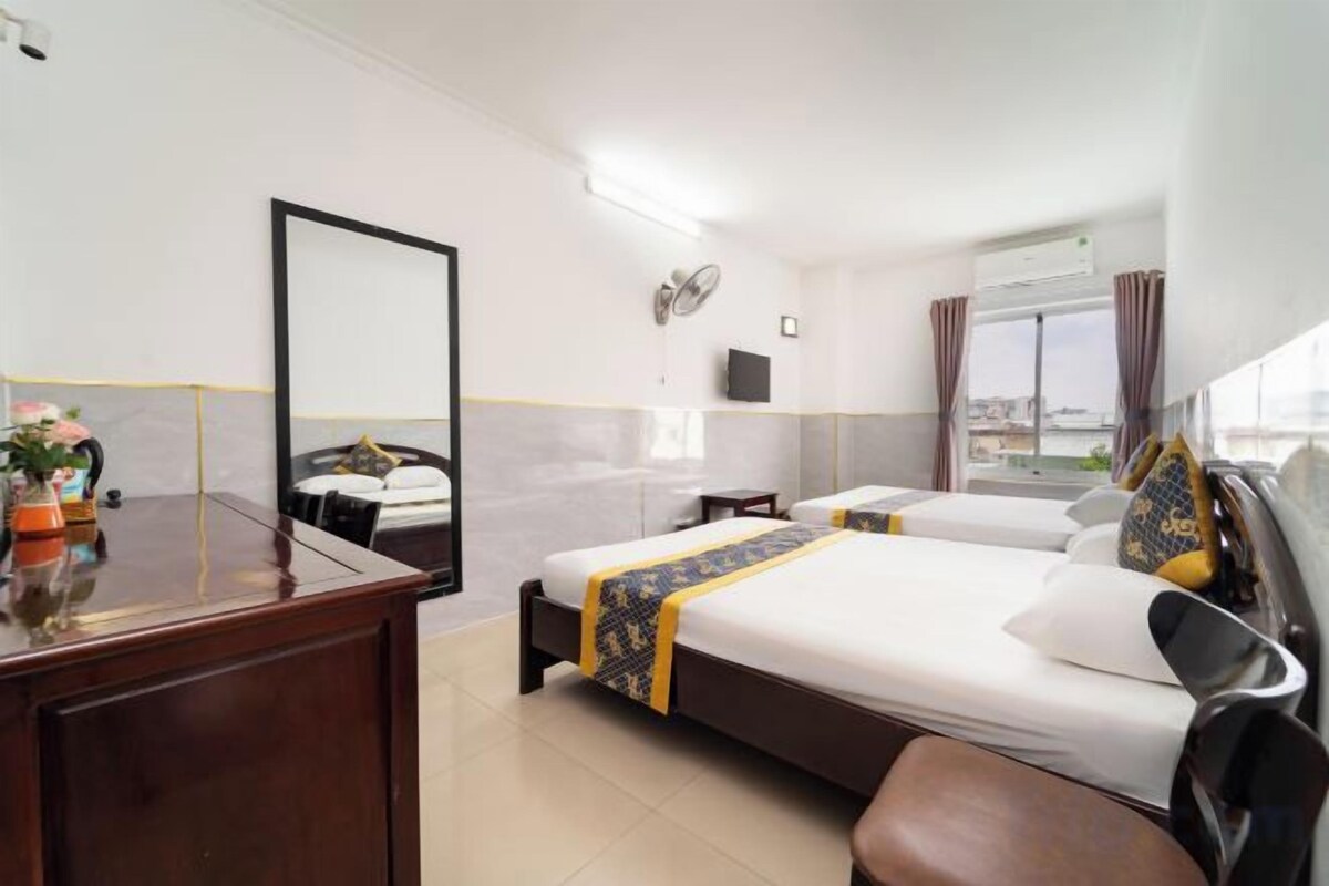 A hotel room with a bed, a desk, a mirror, a window, and a view of the city.