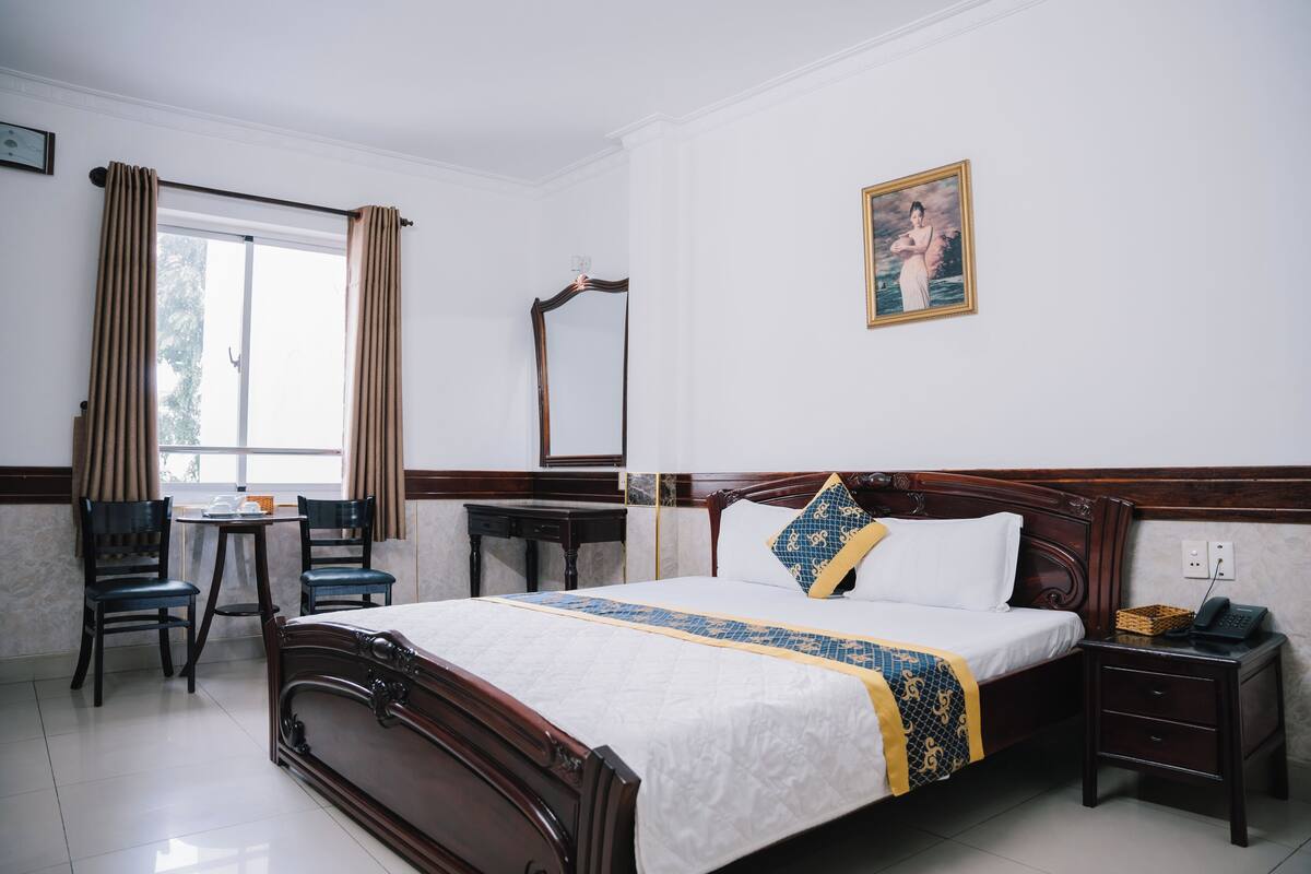 Ein Hotelzimmer mit Bett, Nachttisch, Stuhl und einem Fenster mit Vorhängen.