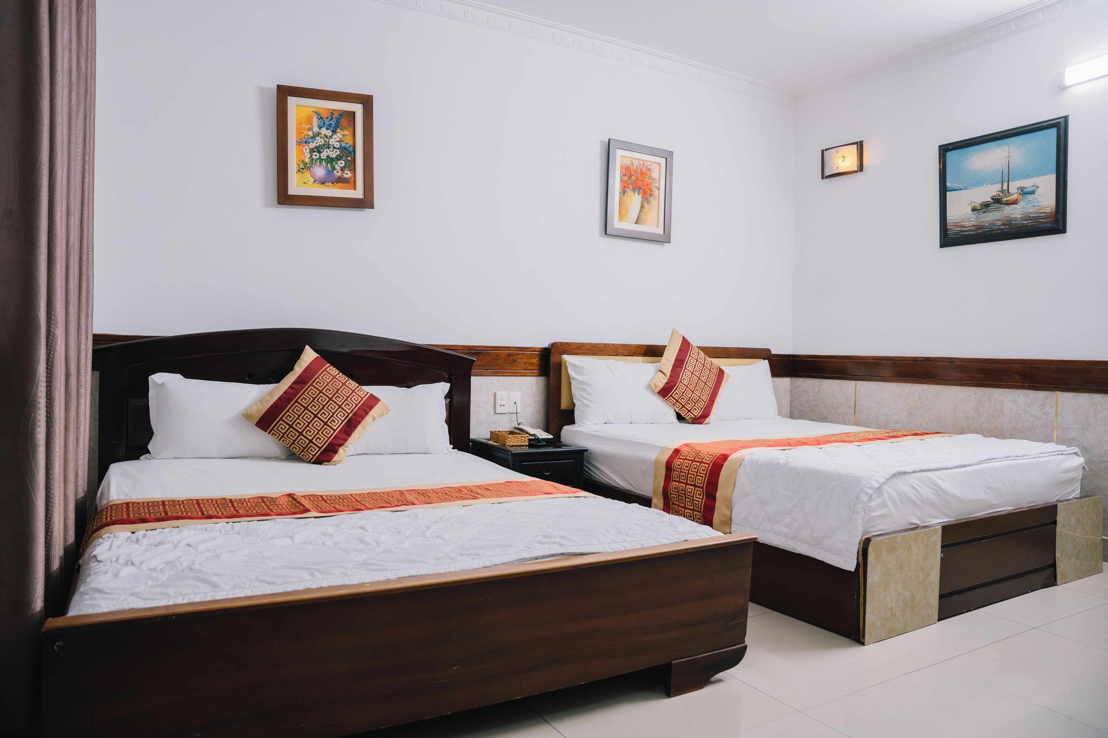 Ein Hotelzimmer mit zwei Betten, weißen Leinen und dekorativen Kissen. An den Wänden befinden sich gerahmte Kunstwerke und ein Nachttisch mit einer Lampe.