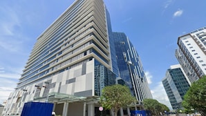 A modern high-rise building with a distinctive angular design, featuring a glass facade and a series of balconies. - 8 Newtown Boulevard by HiveRooms (Lapu-Lapu)