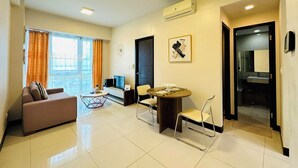 A modern living room with a sofa, a dining table with chairs, a TV, and a large window with curtains. - 8 Newtown Boulevard by HiveRooms (Lapu-Lapu)
